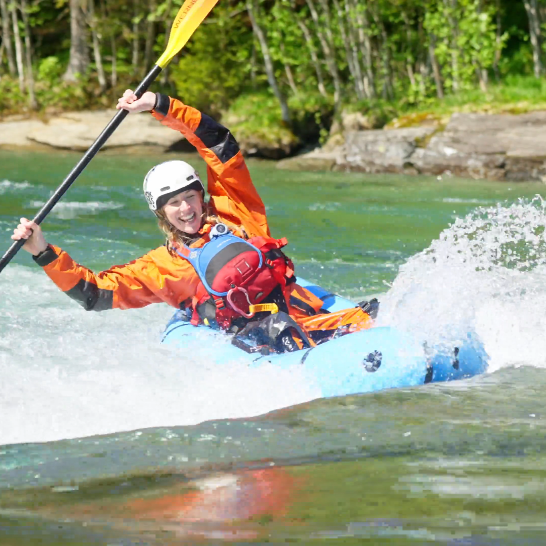 kvinne i en packraft i turkis elv på Voss. båten er vendt oppstrøms og hun forsøker å surfe på en bølge.