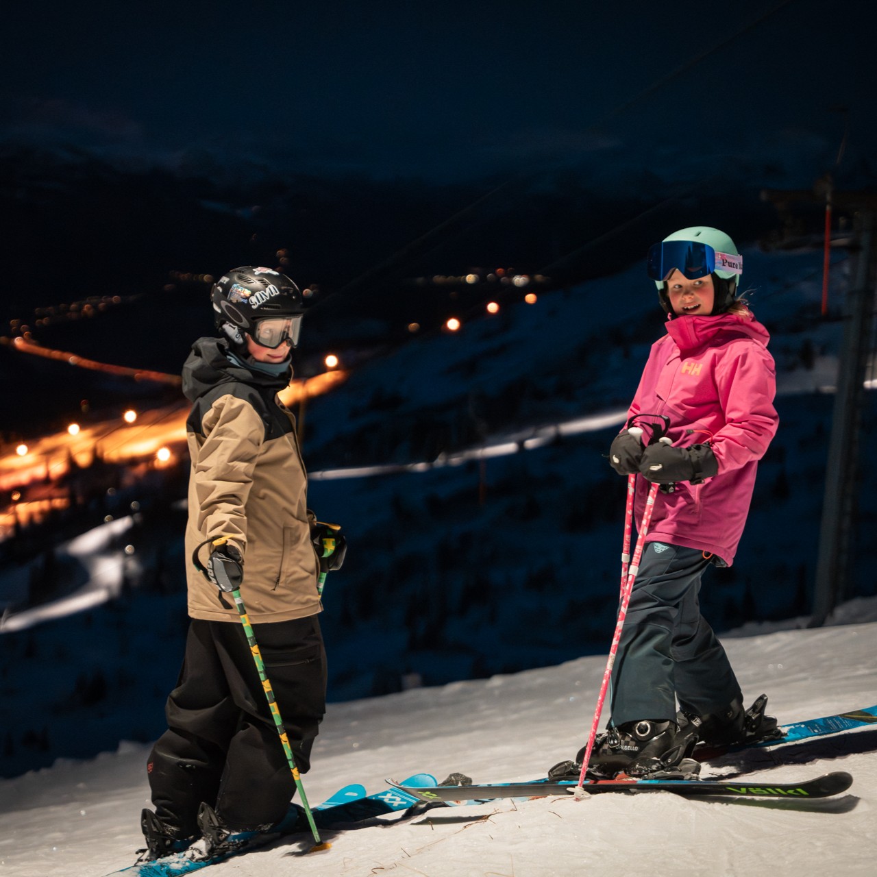 barn i skibakken på kveldskjøring, lyssatte bakker i bakgrunn